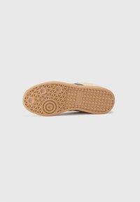 Tan rubber outsole with a geometric pattern, featuring a central circular logo and textured edges for enhanced grip and traction.