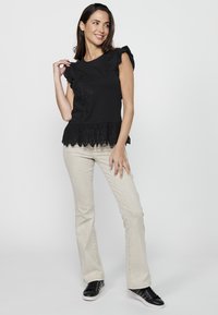 Haut noir à manches courtes avec des manches volantes, broderies florales et un ourlet en dentelle festonnée, associé à un jean flare de couleur claire et des baskets noires.