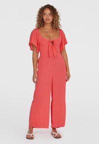 Korallfärgad jumpsuit med korta fladderärmar, en detalj med framslips och vida byxor; tillverkad av lättviktigt tyg för komfort.