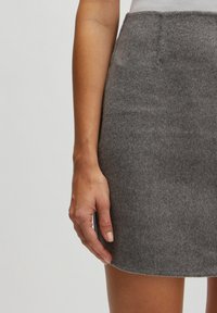 Grauer Woll-Minirock mit glatter Textur, tailliertem Schnitt und leicht ausgestelltem Saum, gezeigt neben einer Hand, die auf dem Stoff ruht.