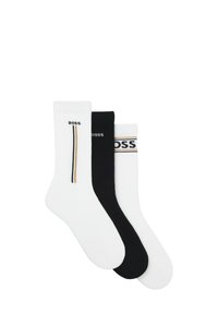 Drei Paar Knöchelsocken in Weiß und Schwarz, jeweils mit "BOSS"-Logo und gestreiften Details am Bündchen oder an der Seite.