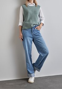 Ljusgrön stickad väst över en vit skjorta med knappar, kombinerad med ljusblå vida jeans och vita sneakers. Texturerade tyger och avslappnad passform.