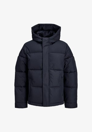 Tengerés kék puffermellény cipzárral és kapucnival, világos pólóval és szürke melegítőnadrággal párosítva. Párnázott részekkel és rugalmas mandzsettákkal rendelkezik.