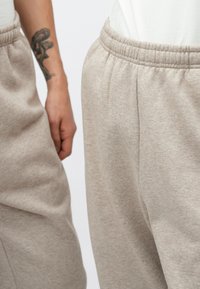 Ανοιχτό μπεζ παντελόνι φόρμας κατασκευασμένο από απαλό, υφασμένο ύφασμα, με ελαστική μέση και πλαϊνές τσέπες. Ο σχεδιασμός περιλαμβάνει λεπτές ραφές.