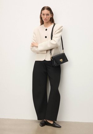 Smėlio spalvos struktūruotas švarkas su juodais mygtukais, juodos plačiomis kojomis kelnės ir juoda rankinė su auksinėmis detalėmis. Lygūs, modernūs audinių apdailos elementai.