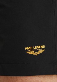 Čierne šortky vyrobené z hladkej tkaniny s žltým vyšitým logom PME Legend s krídlami, umiestneným blízko lemu.