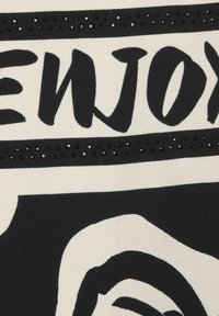 Zwart-witte stof met gedurfde grafische tekst en een gladde textuur, met een rij kleine zwarte versieringen langs het ontwerp.