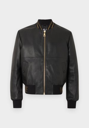 Veste aviateur en cuir noir avec fermeture éclair dorée, col et poignets côtelés, deux poches avant et détails brodés sur la ceinture.