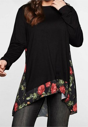 Haut noir à manches longues avec un ourlet floral mettant en avant des roses rouges et des feuilles vertes. Tissu doux, design asymétrique et coupe décontractée.