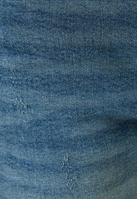 Tessuto di denim azzurro chiaro con una trama testurizzata, caratterizzato da piccole aree sfilacciate e sottili variazioni di colore.