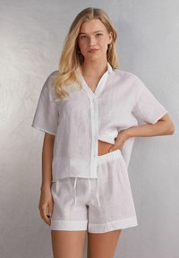 Vit linneskjorta med kort ärm, knappstängning framtill med krage, tillsammans med matchande vita linneshorts med resårmidja.