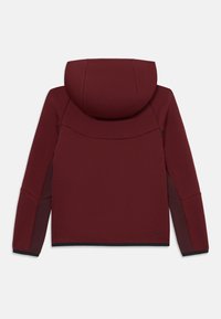 Casaco com capuz e mangas longas em vermelho escuro com detalhes em preto, visto por trás, apresentando um design contornado e o logotipo da Nike próximo à bainha inferior.