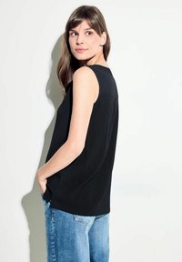 Top nero senza maniche con una trama texturizzata, vestibilità leggermente ampia e scollo rotondo, abbinato a jeans in denim blu chiaro.