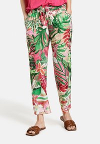 Leichte Hose mit Blumenmuster in Grün-, Pink- und Beigetönen; elastischer Bund und Seitentaschen. Kombiniert mit braunen Slide-Sandalen.
