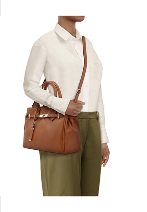 Sac à main en cuir marron avec deux poignées et une longue bandoulière, doté de ferrures argentées et d'un design texturé. Porté avec un haut clair.