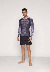 Langarm rashguard met een zwart en grijs ontwerp met grafische patronen, gecombineerd met zwarte zwemshorts. Soepele textuur, sportieve pasvorm.