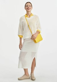 Biały sweter z dzianiny założony na żółtą koszulę z kołnierzykiem, w komplecie z białą spódnicą dzianinową z bocznym rozcięciem i beżowymi trampkami. Żółta torebka na ramię.
