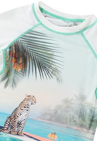 Īsas piedurknes rash guard gaiši zilā krāsā ar zaļu apdari, kurā attēlots leopardu sērfojot uz sērfošanas dēļa, palmu lapas un tropiskais fons.