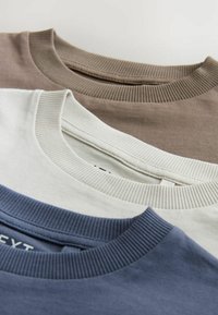 Trois T-shirts empilés : un en gris clair, un en marron sourd et un en bleu marine. Chacun a un col rond côtelé et une texture en coton lisse.