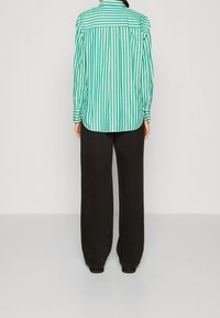 Camicia a righe verdi e bianche con orlo curvo, maniche lunghe e pantaloni neri a gamba larga. Texture liscia, design casual.