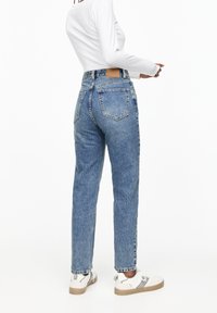 Jeans en denim bleu clair taille haute, avec cinq poches, coupe droite et une étiquette en cuir beige sur la ceinture arrière.