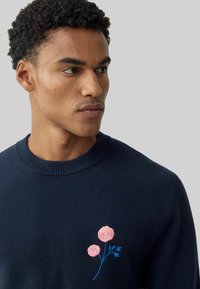 Pulover bleumarin cu decolteu rotund striat, decorat cu broderie florală roz și accente albastre. Textură moale, croială ajustată.