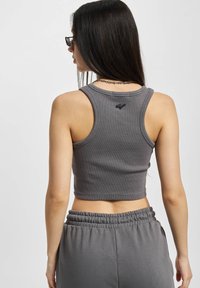 Sivi uski top s cropped krojem napravljen od rebraste tkanine, koja prikazuje blagu teksturu i mali logotip na stražnjem dijelu, u kombinaciji sa sivim trenirkama.