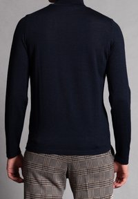 Marinefarbener Langarm-Turtleneck aus leichtem Stoff, mit strukturiertem Rippdesign und figurbetontem Schnitt, kombiniert mit karierten Hosen.