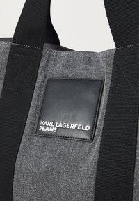 Graue Stofftasche mit schwarzen synthetischen Lederakzenten. Verfügt über breite schwarze Träger und ein Logopatch mit der Aufschrift "KARL LAGERFELD JEANS."