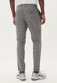 Pantaloni grigi a quadri con vestibilità slim, dotati di tasche posteriori e una texture liscia. Abbinati a scarpe da ginnastica argento e blu.