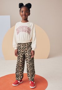 Felpa bianca con la scritta "Happiness" in rosa, abbinata a pantaloni larghi con stampa leopardata. Sneakers rosse e acconciatura con due chignon completano il look.