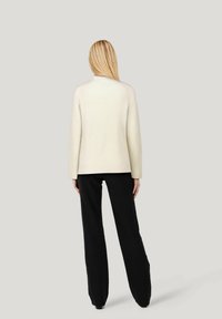 Rippiger cremfarbener Pullover mit hohem Kragen und langen Ärmeln, kombiniert mit schwarzen, schmal geschnittenen Hosen. Einfaches und minimalistisches Design.