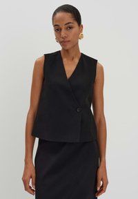 Schwarzes ärmelloses Wickeltop mit tiefem V-Ausschnitt und einem einzelnen Knopfverschluss, das ein klar geschnittenes Design und einen strukturierten Stoff aufweist.