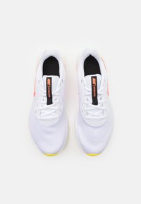 Běžecké boty Nike s bílou síťovinou, černým vnitřním podšitím, jasně oranžovými akcenty na stranách a žlutou gumovou detailní podešví.