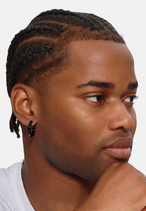 Orecchino a cerchio nero con superficie texture, indossato da una persona con capelli trecciati. Il tono della pelle è medio, con una texture liscia e un'espressione neutra.