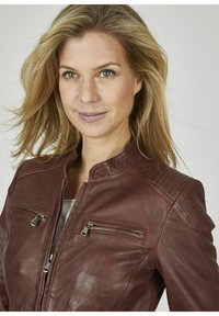 Braune Lederjacke mit minimalistischem Design, ausgestattet mit einem Stehkragen, zwei Reißverschlusstaschen und strukturierten Details an den Schultern.