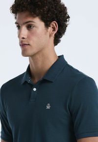 Navyblaues Poloshirt aus einem weichen Baumwollgemisch mit einer Drei-Knopf-Leiste. Mit einem gestickten Pinguin-Logo auf der linken Brust.