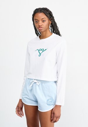 Crop top alb cu manșon lung și un design grafic verde; asortat cu șorturi deschise la culoare, cu șnur, având un logo brodat.