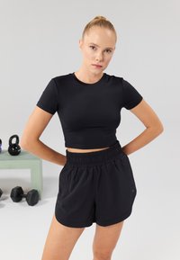 Musta urheilullinen cropped toppi, joka on valmistettu joustavasta materiaalista, yhdistetty mustiin elastisiin shortseihin. Yksinkertainen muotoilu, sileä pinta ja ei näkyviä kuvioita.
