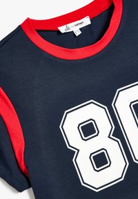 Camiseta de color navy con cuello y acentos en las mangas en rojo, con un gran gráfico blanco "80" en el frente. Hecha de suave tela de algodón.