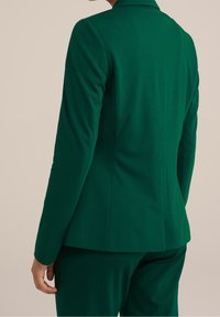 Zelený přiléhavý blazer vyrobený z hladkého materiálu. Má výstřih ve tvaru klopy, dlouhé rukávy a propracovaný siluetu s detailem švů.