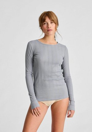 Długi rękaw, jasnoszara bluzka o ryflowanej teksturze, okrągłym dekolcie i dopasowanym kroju. Posiada długie rękawy z otworami na kciuki dla dodatkowego komfortu.