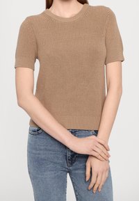 Brun, ribbad kortärmad stickad tröja med rund halsringning. Strukturerad textur och figurnära silhuett, i kombination med blå denimjeans.