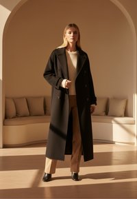 Zwart dubbelzijdig wollen jas met grote revers, gedragen over een crèmekleurige geribde trui en beige broek, gecombineerd met zwarte enkellaarsjes.