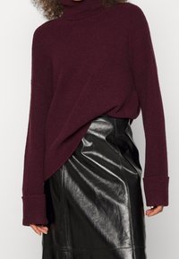 Burgundy polokrage i ribbad stickad kvalitet, med översize ärmar, i kombination med en figurnära svart läderkjol med glansig finish.