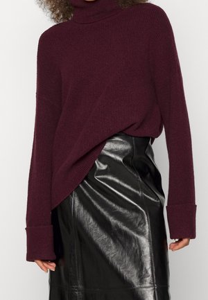Pull à col roulé bordeaux en tricot côtelé, avec des manches surdimensionnées, associé à une jupe en cuir noir ajustée à finition brillante.