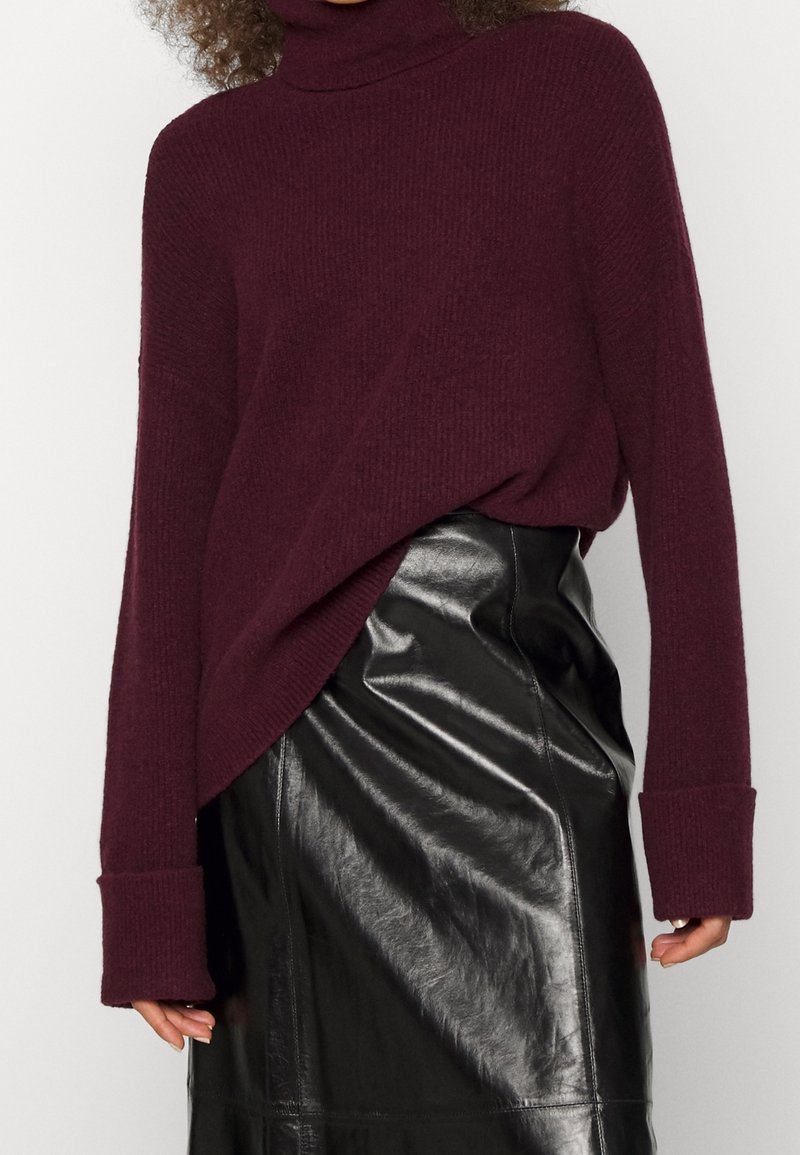 Burgundy polokrage i ribbad stickad kvalitet, med översize ärmar, i kombination med en figurnära svart läderkjol med glansig finish.