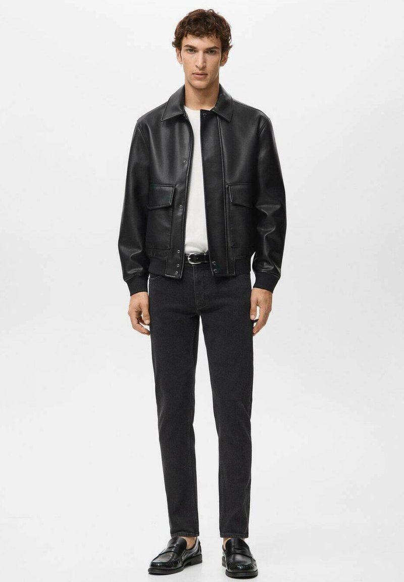 Schwarze Lederjacke mit Kragen, ausgestattet mit zwei Fronttaschen. Trägt man über einem weißen Hemd, kombiniert mit schwarzer Jeans und Schuhen.