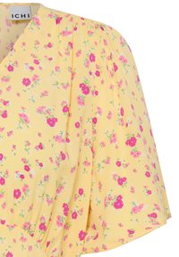 Tissu jaune avec un petit imprimé floral rose et magenta, avec une manche ballon froncée et une étiquette de marque ICHI visible.