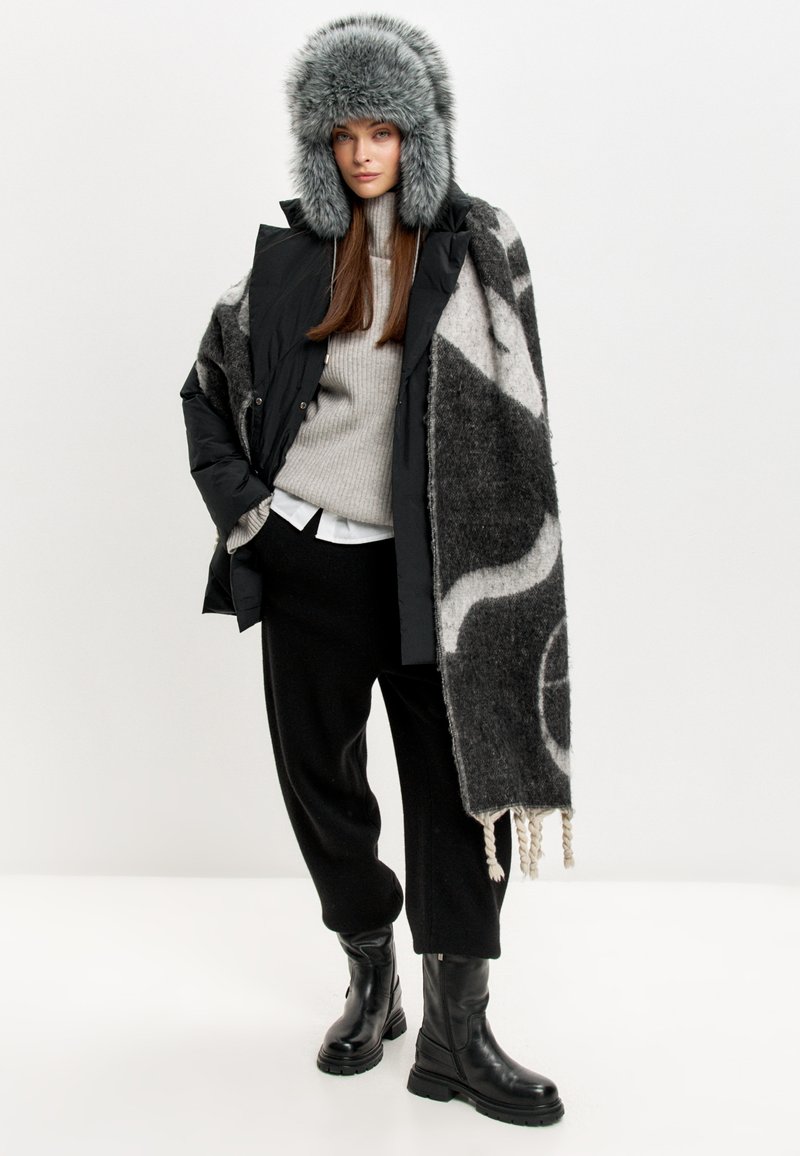 Giacca a vento nera, maglione grigio a maglia, pantaloni neri a gamba larga, stivali neri alti e un cappello grigio in pelliccia sintetica. Avvolto in una coperta grigia a fantasia.